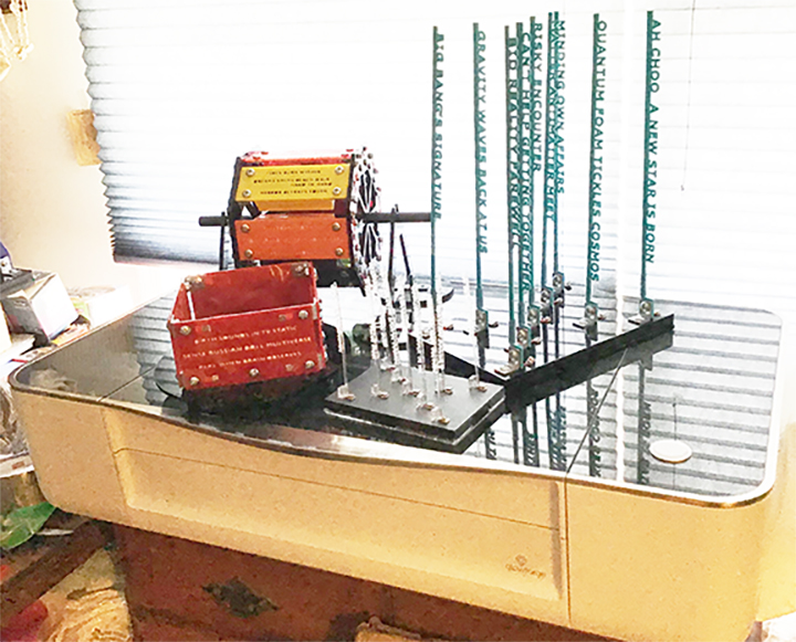 Image shows four tactile mixed media art pieces that can "talk" when buttons are pressed.  Upper left is the Ferris Haiku work, lower left shows Merry-Go-Round Haiku piece, lower right shows small version of larger piece on right rear showing two Tanka poems with same middle line in X shape.  All four pieces are sitting on top of a Glowforge 3D laser cutter.